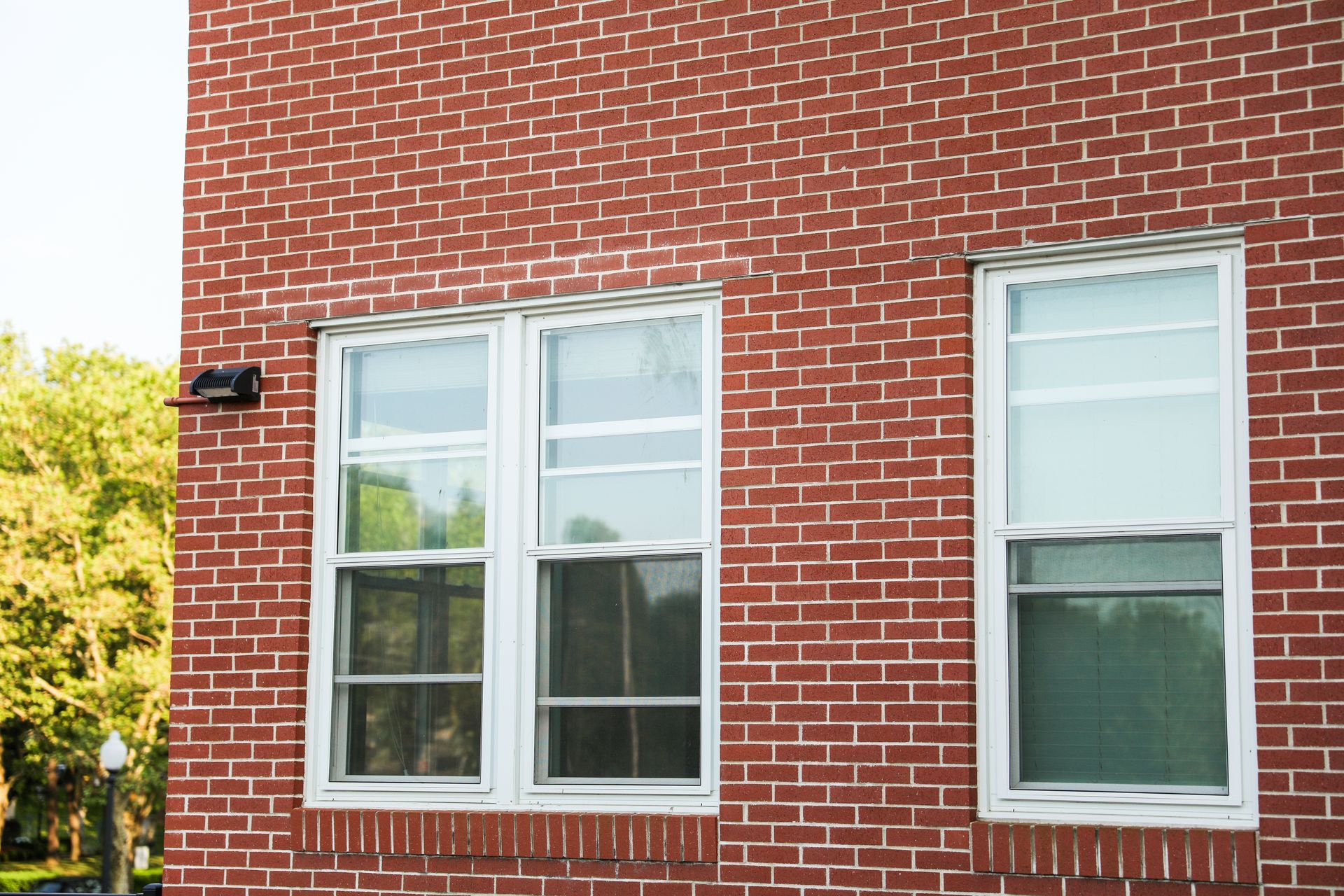 Red brick building with two white-framed windows. A small black box sits above the left window.
