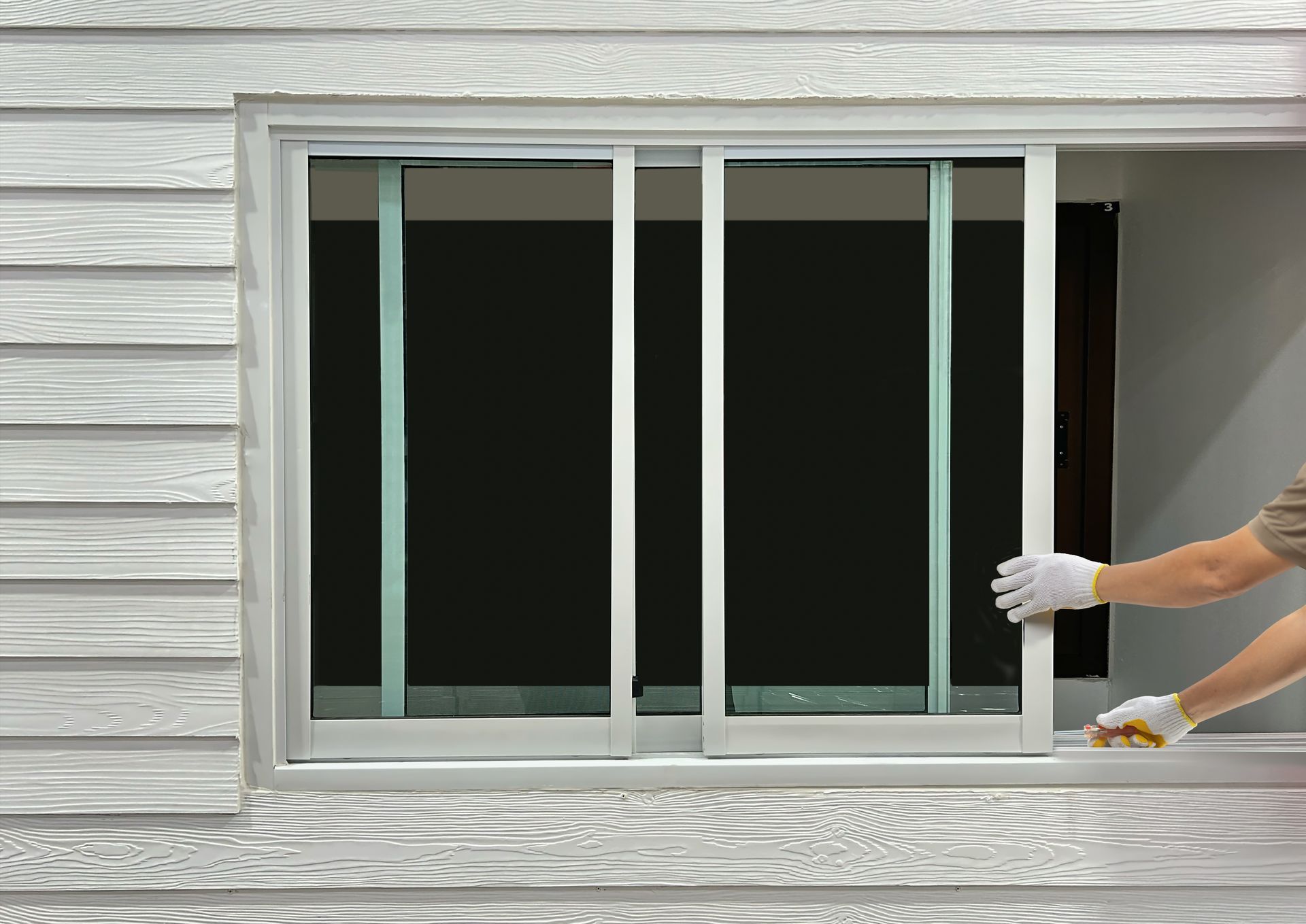 Person in gloves removing a sliding window from a white-sided building.