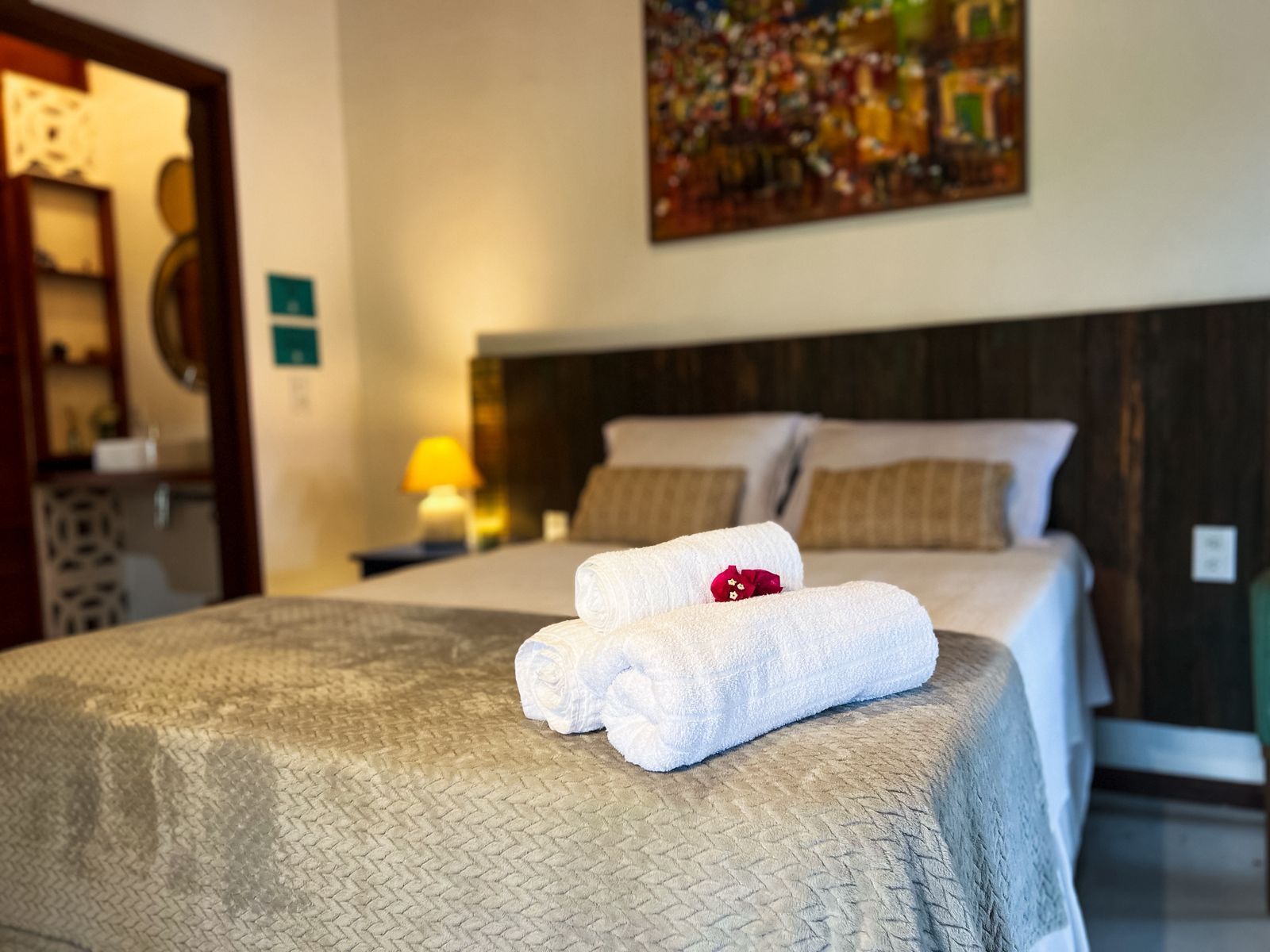 Quarto de hotel com cama arrumada, toalhas dobradas e abajur aceso.