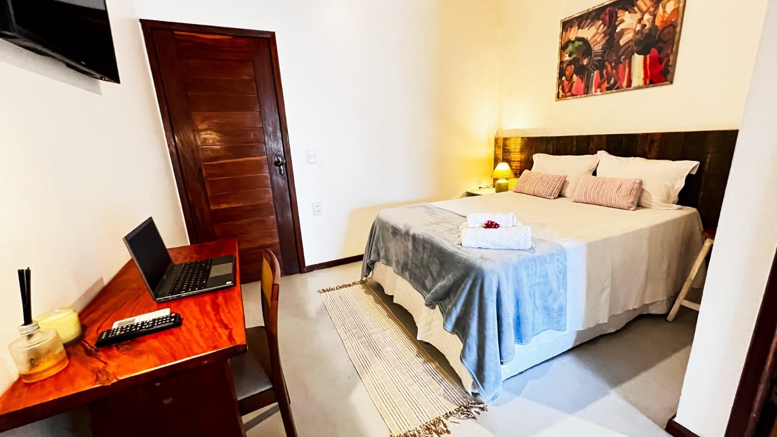 Quarto aconchegante com cama, abajur, guarda-roupa de madeira, escrivaninha e obras de arte na parede.