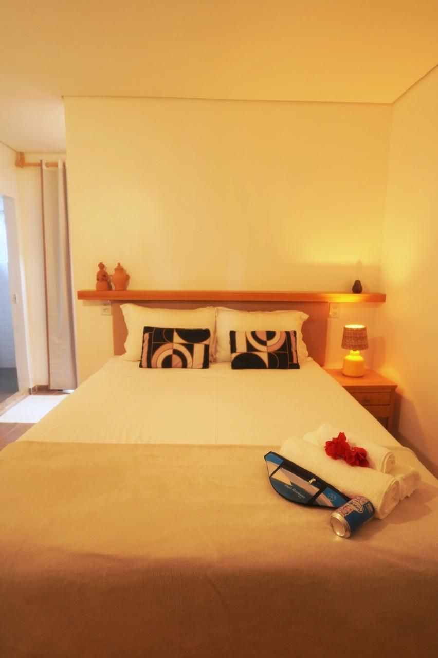 Quarto aconchegante com cama arrumada, cabeceira de madeira e um abajur aceso na mesa de cabeceira.