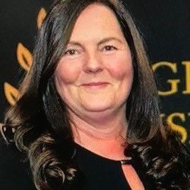 Woman with brown hair smiling, wearing a black top, against a gold and black backdrop.