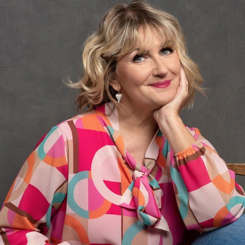 Woman in colorful blouse with hand on chin, smiling.