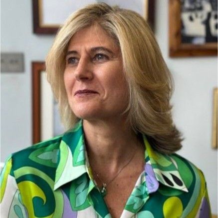 Woman with blonde hair wearing a green patterned shirt, looking to the side with a slight smile, indoors.