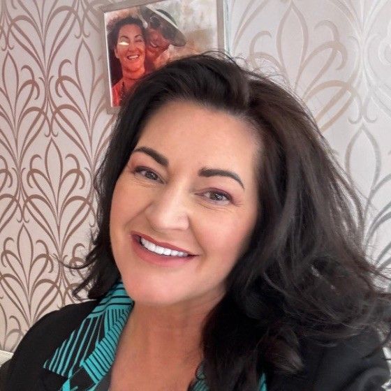Woman with dark hair smiles; floral wallpaper background.
