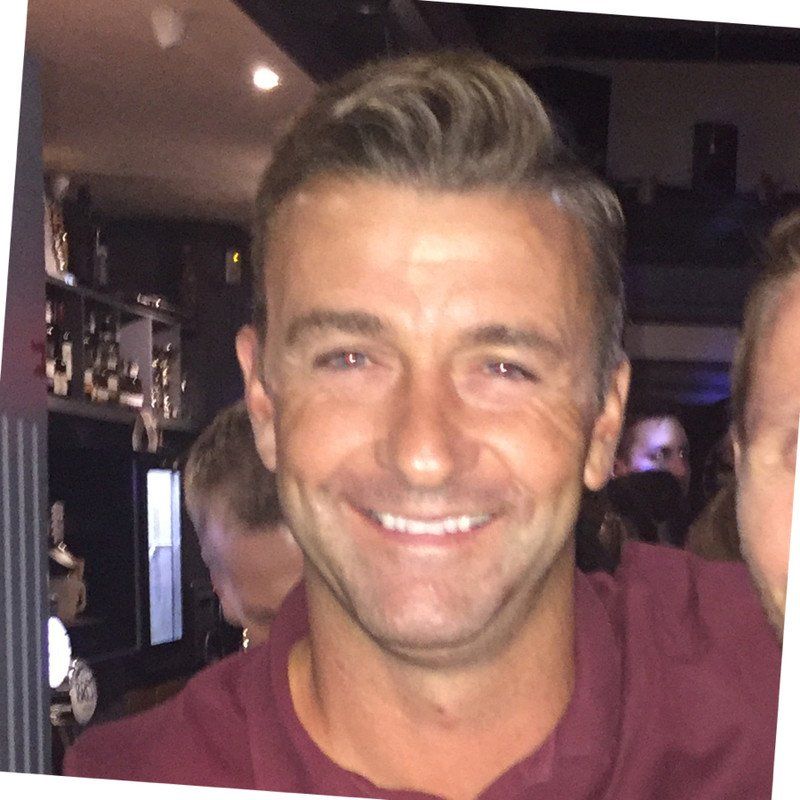 Smiling man with short, styled hair; wearing a maroon shirt. In a bar setting.