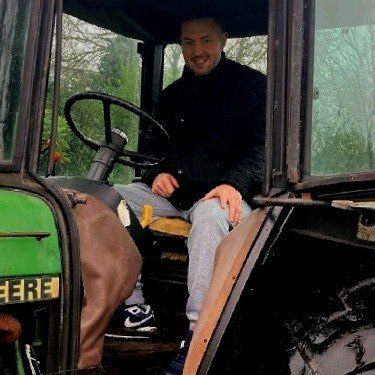 Man sitting in the driver's seat of a John Deere tractor, smiling.
