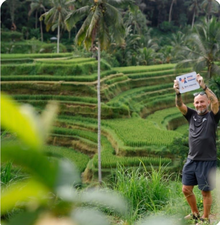 Man in athletic wear holding a sign, posing in front of rice terraces in Bali, Indonesia.