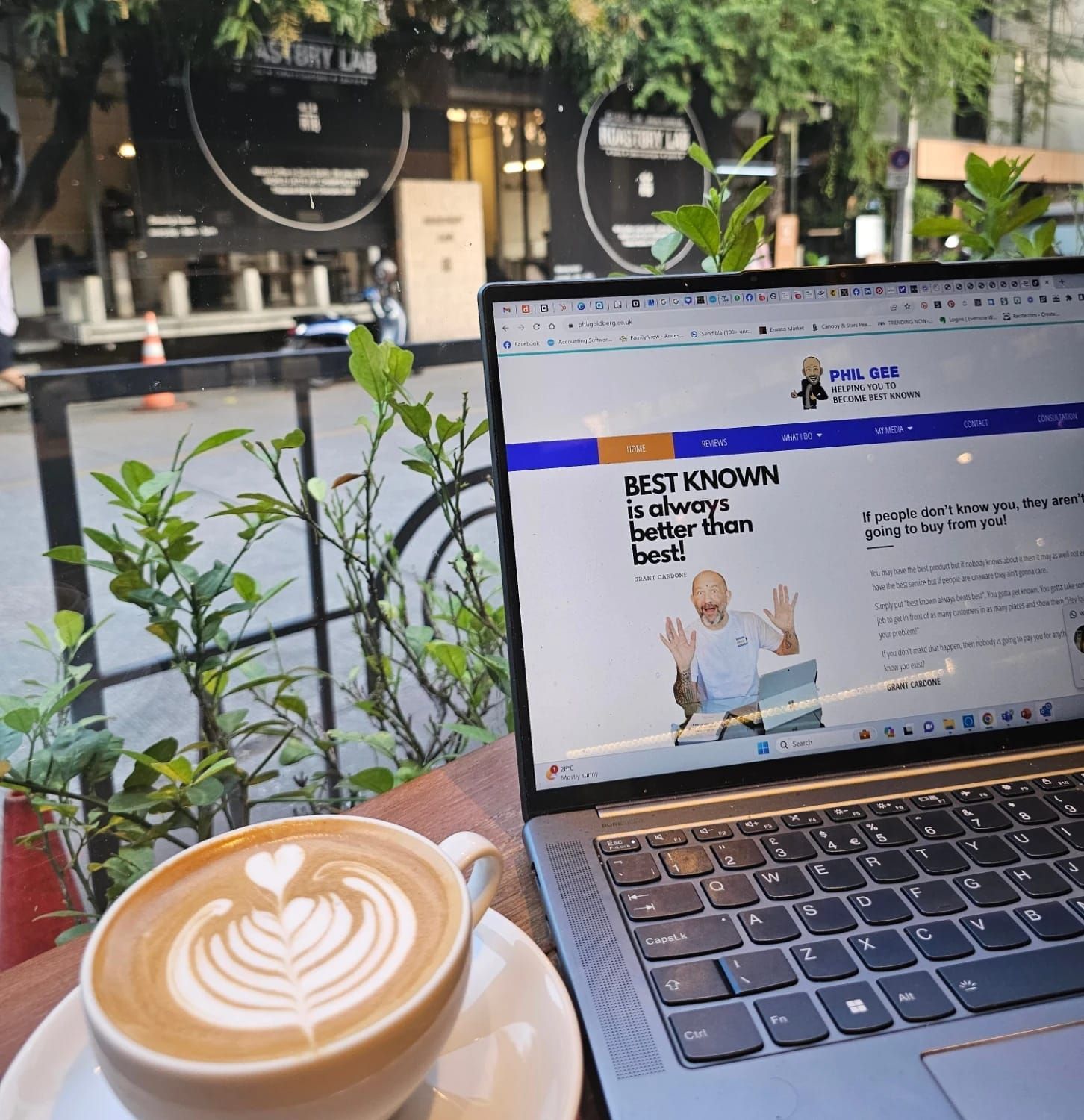 Laptop displaying website, latte art, outdoors setting.