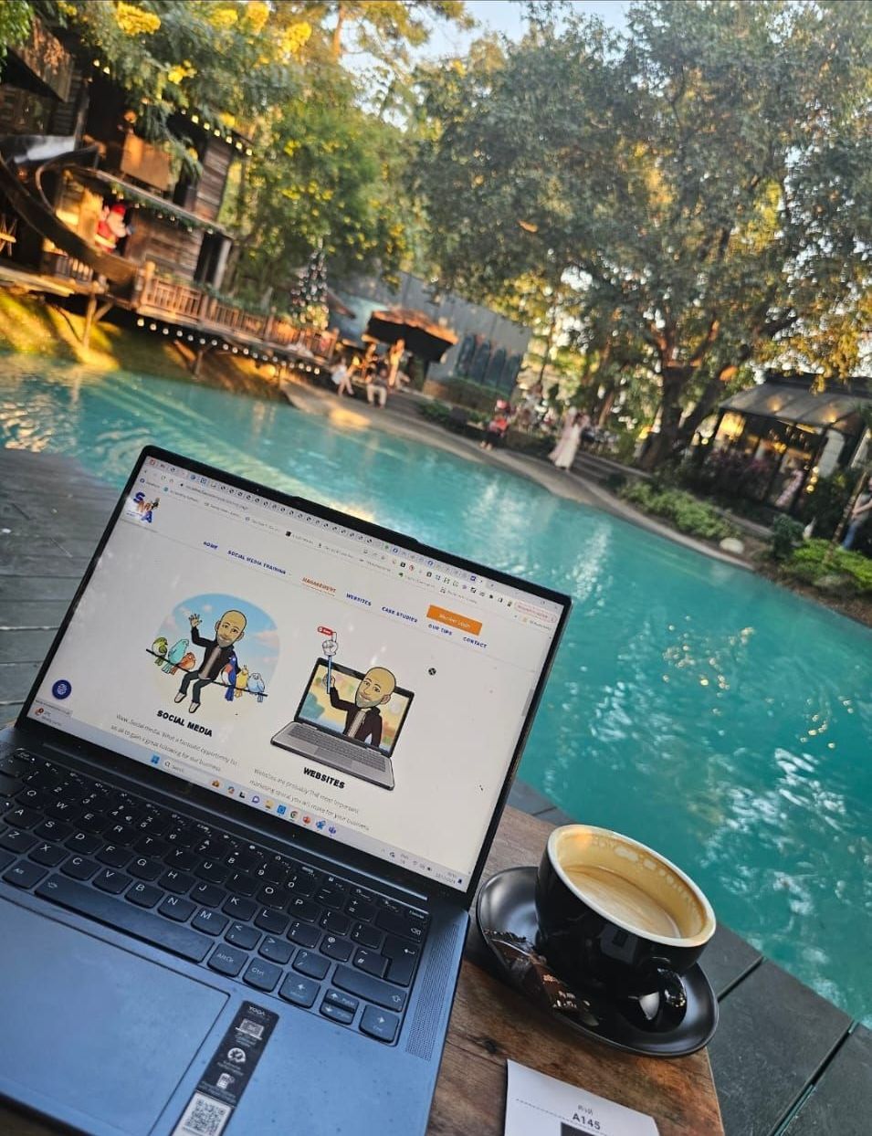 Laptop open next to coffee cup, overlooking pool. Website displayed, outdoor setting.