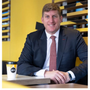 Man in suit smiles, sitting at McDonald's table with coffee cup. Yellow wall background.