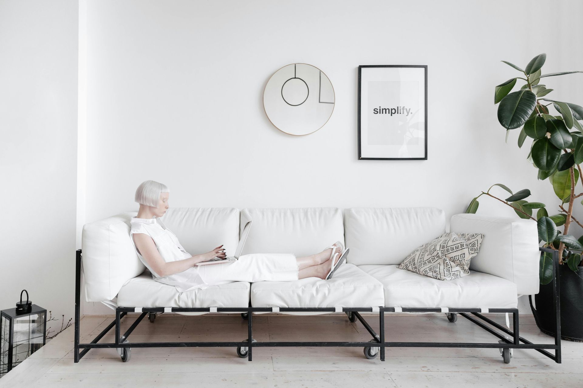A woman is sitting on a white couch using a laptop.