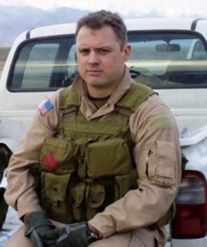 A man in a military uniform is sitting in front of a white truck