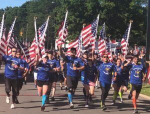 A group of people are running down a street holding american flags.