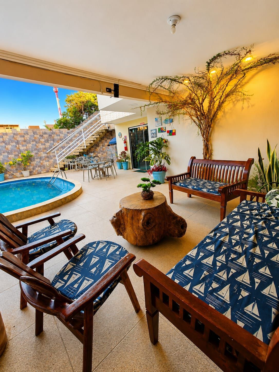 Pátio coberto com piscina azul, cadeiras de madeira, mesa estampada e vista para a montanha ao pôr do sol.