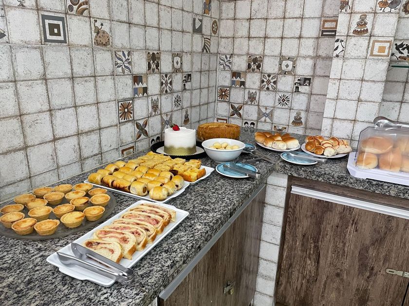 Bandeja com diversos tipos de doces e pães sobre a bancada da cozinha, encostada em uma parede de azulejos.