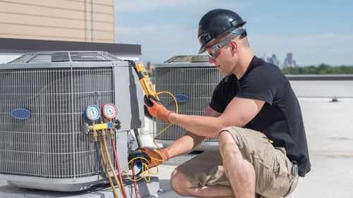 A man is working on an air conditioner on the roof of a building.