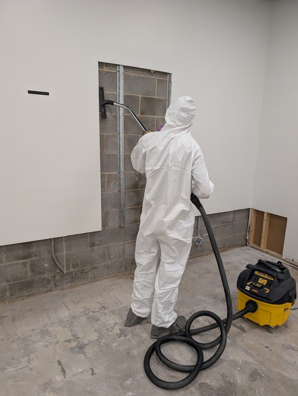 A person in a protective suit is cleaning a microwave in a kitchen.