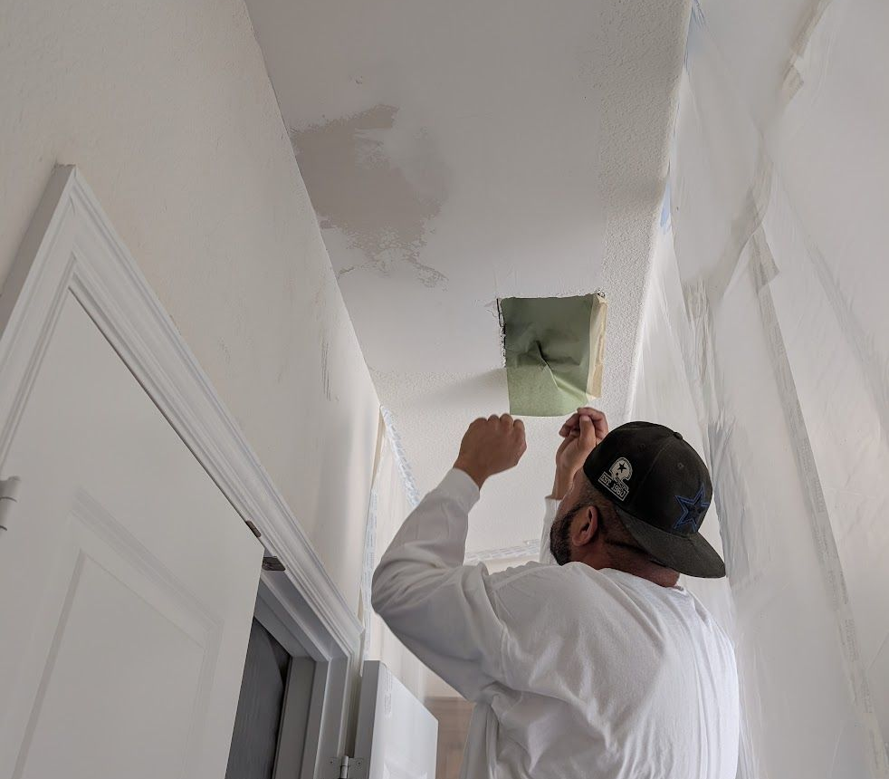 Worker patching drywall on a hallway ceiling near a doorway