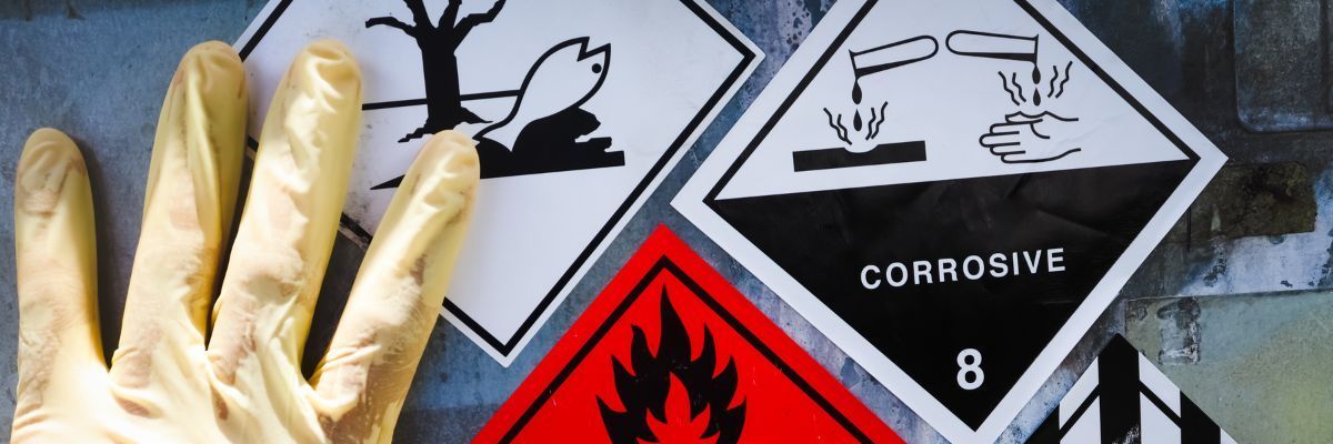 Yellow gloved hand next to hazard warning signs, including