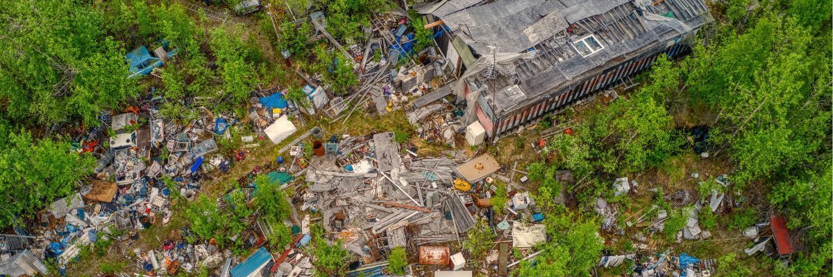 Aerial view of a heavily littered area, with trash and a partially visible structure among green vegetation.