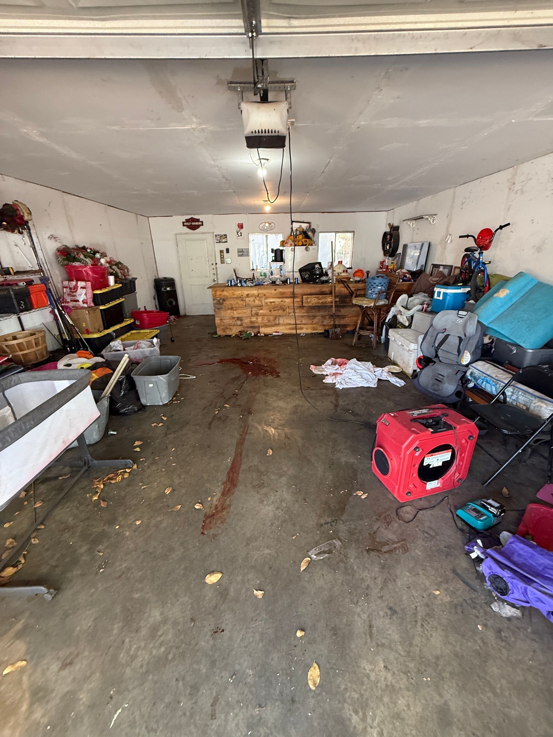 A cluttered, dimly lit garage interior with a wood-topped counter in the back, debris on the concrete floor.