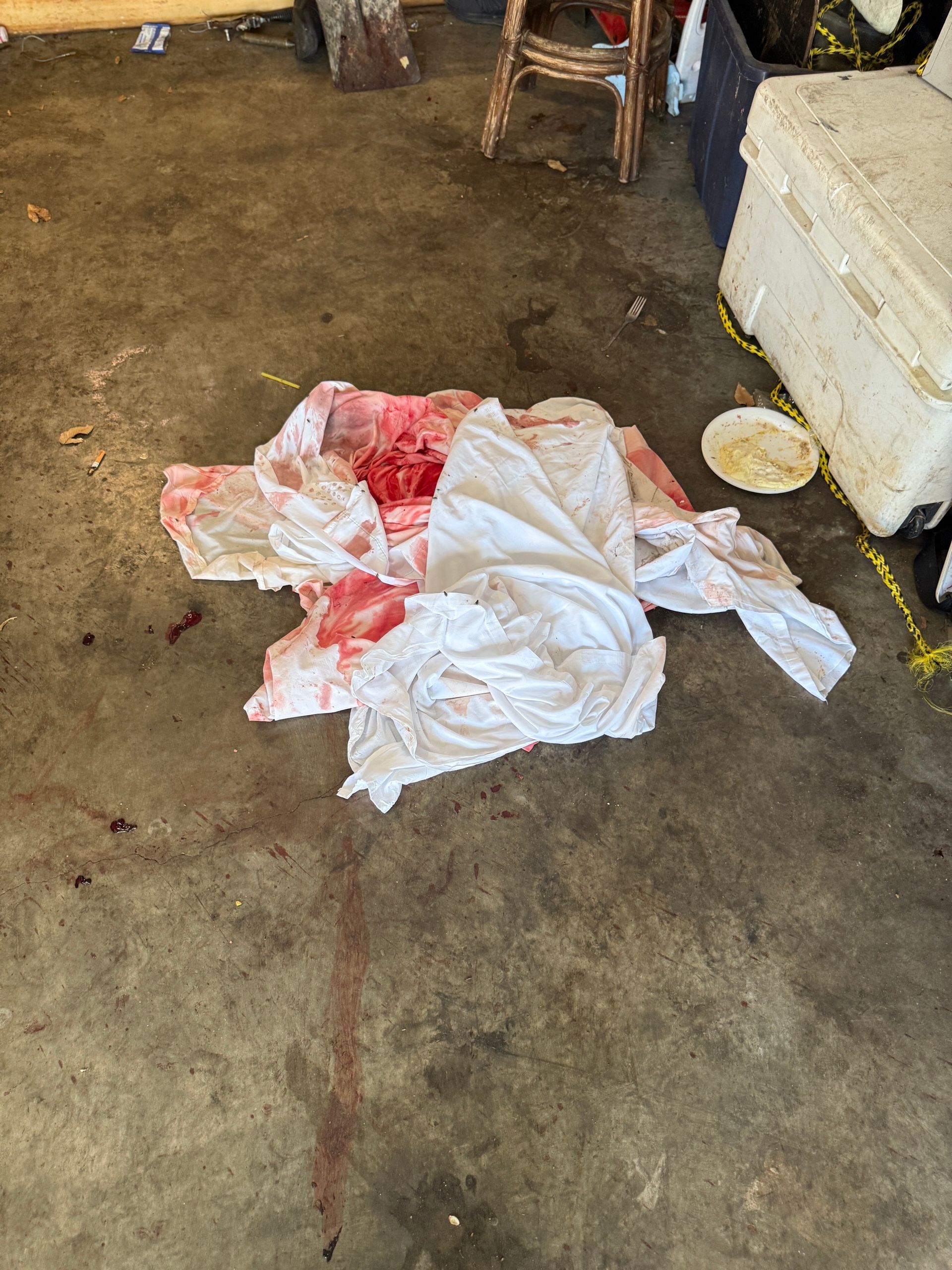 A blood-stained white cloth lies on a concrete floor near a cooler and a wooden stool