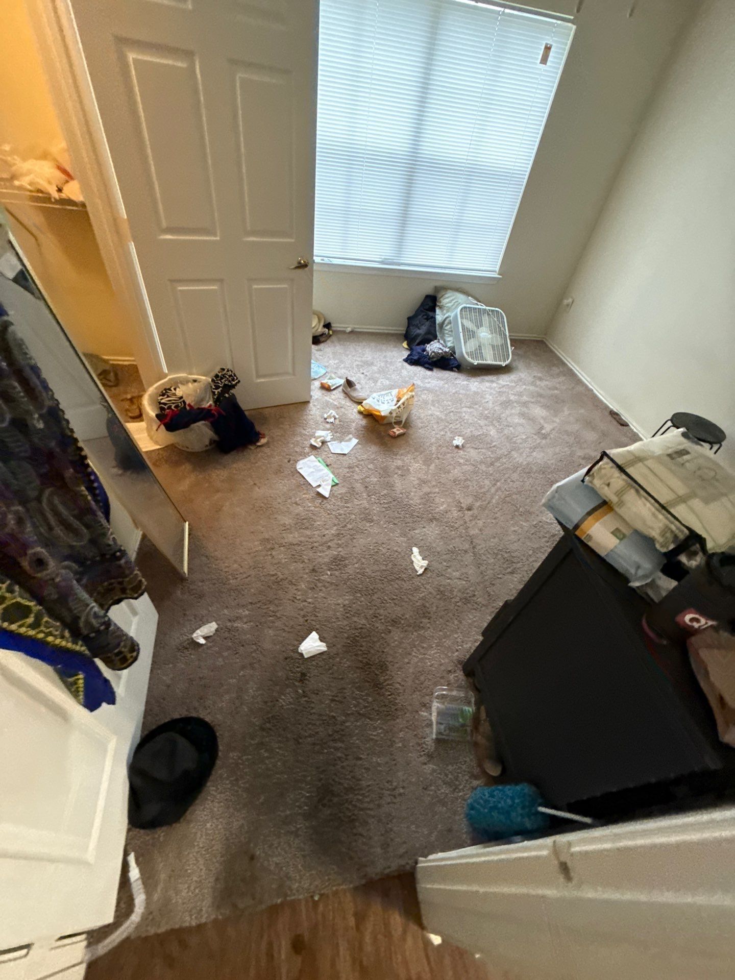Apartment bedroom with belongings and debris on the floor before cleanup