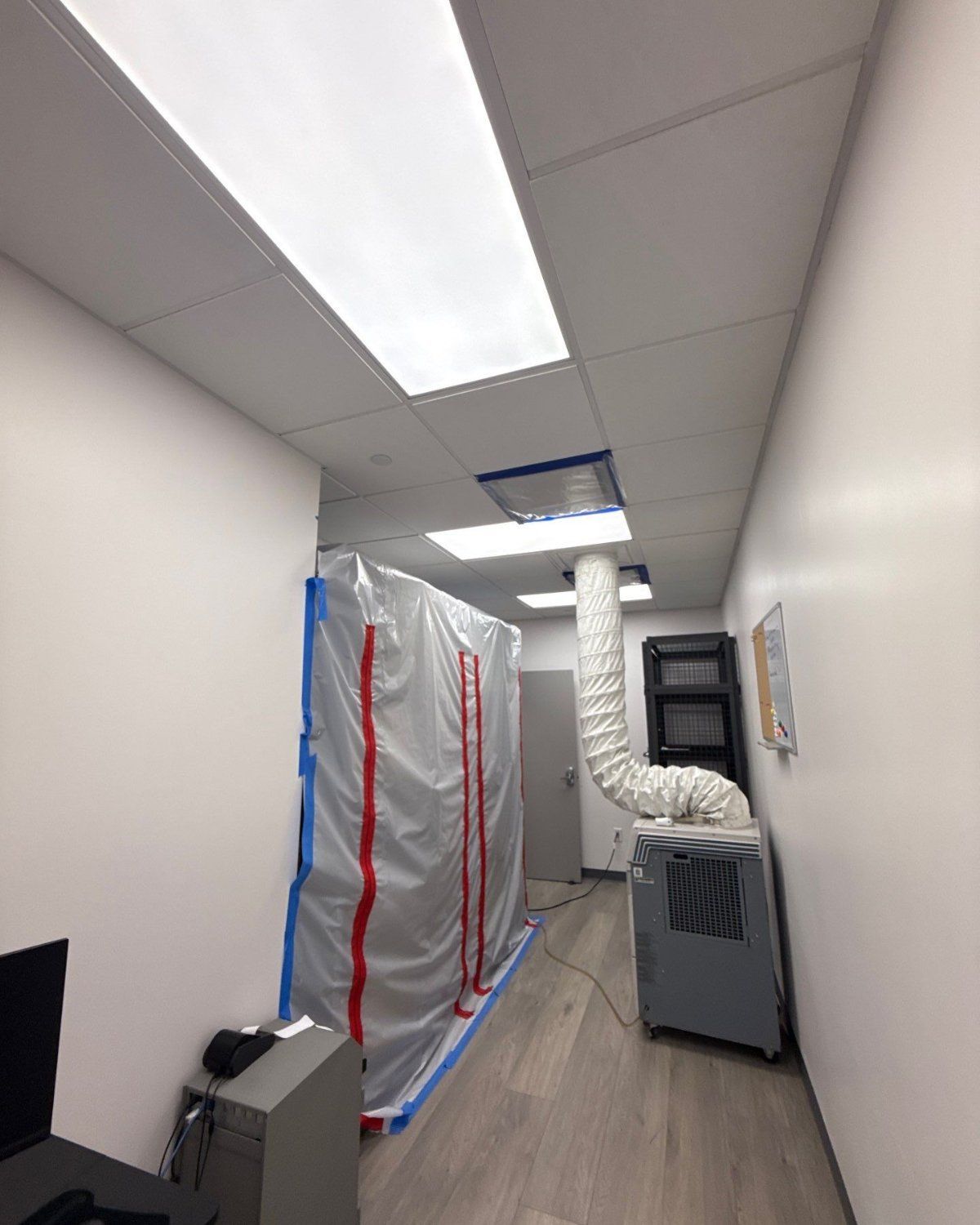 Plastic containment walls with a zipper door and HEPA air scrubber duct in a Plano office hallway