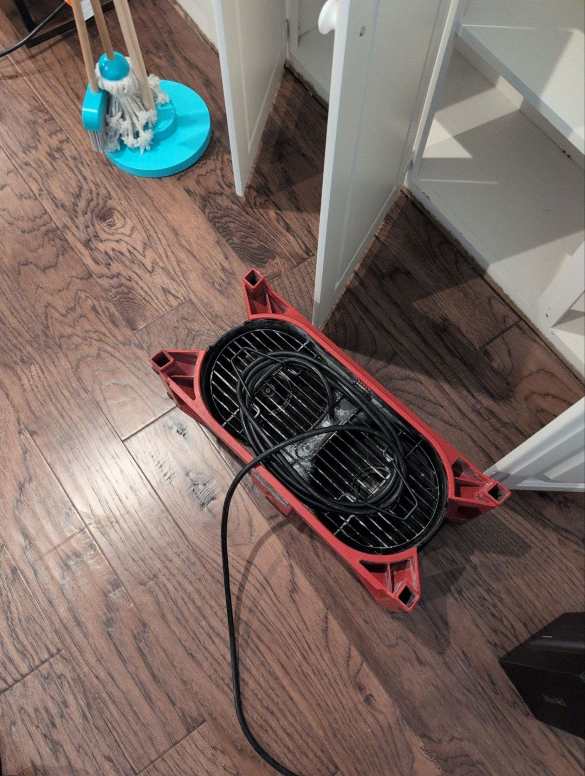 Air mover drying the edge of a hardwood floor beside built-in cabinets