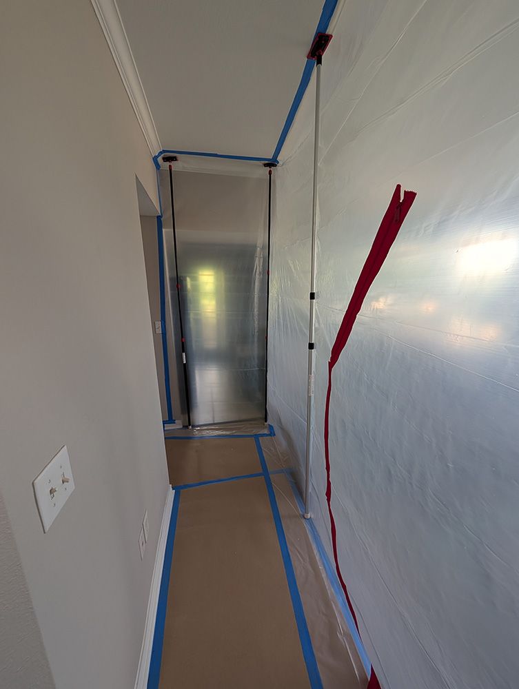 Hallway prepped for painting: plastic sheeting taped to walls, floors covered, masking tape along edges.