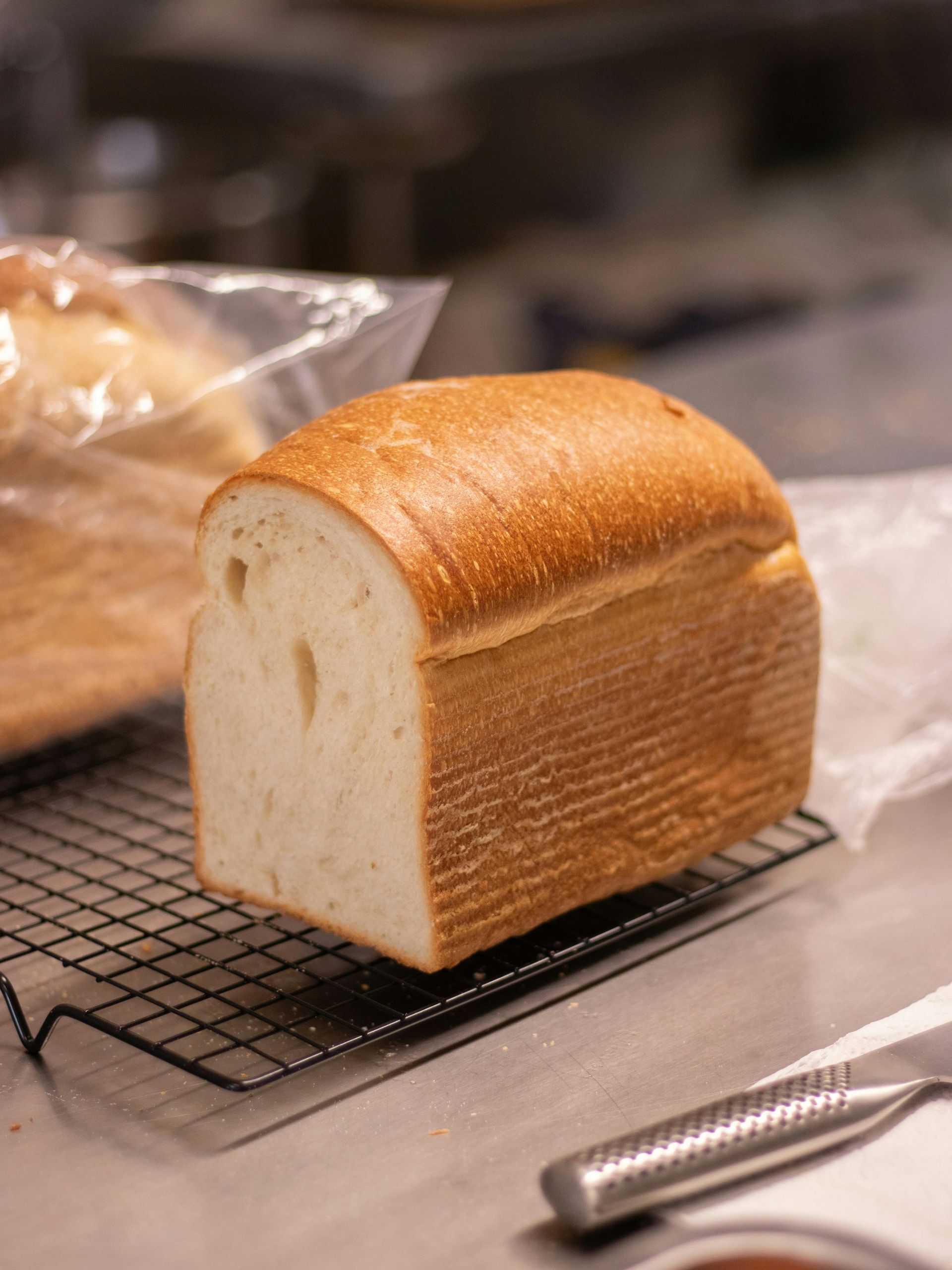 Sliced loaf of golden-crusted bread on a cooling rack, with more bread in the background.