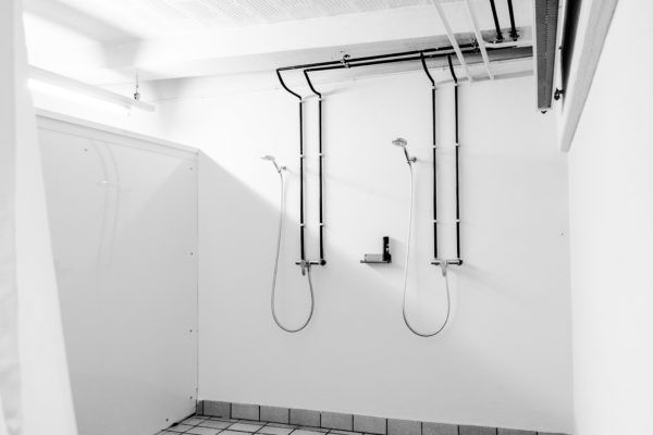 Zwei Duschkabinen mit an einer weißen Wand montierten Rohren und Duschköpfen.