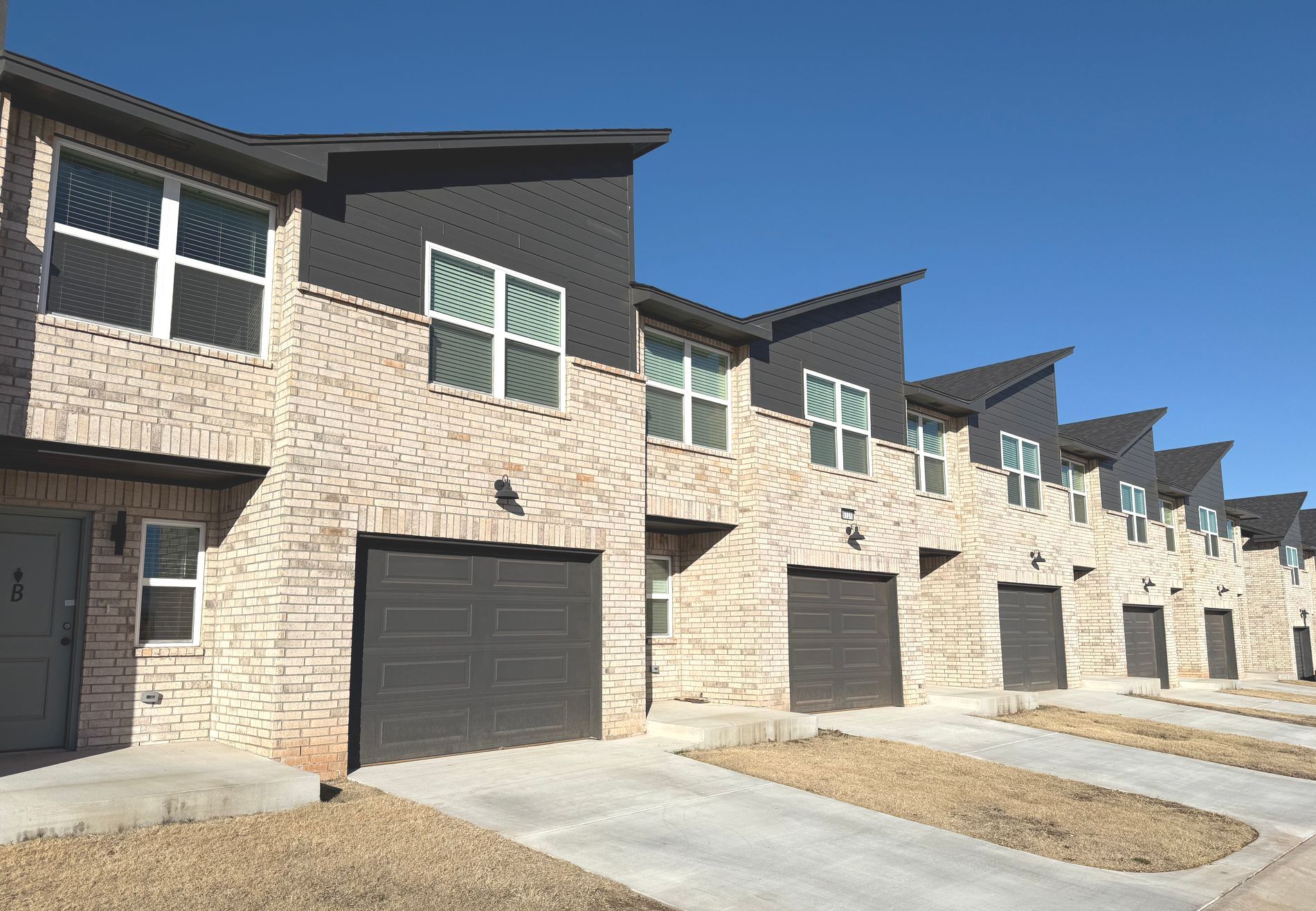 Row of modern tan brick townhouses with dark garage doors under a clear blue sky