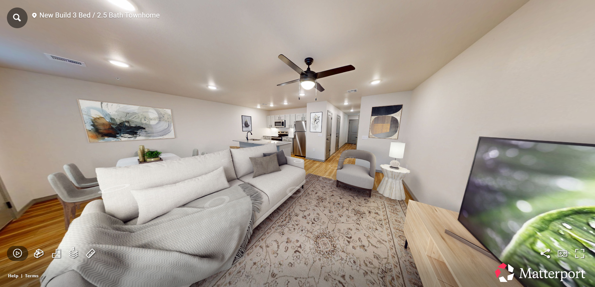 Bright living room with gray sofas, rug, ceiling fan, and TV in a modern open-concept space