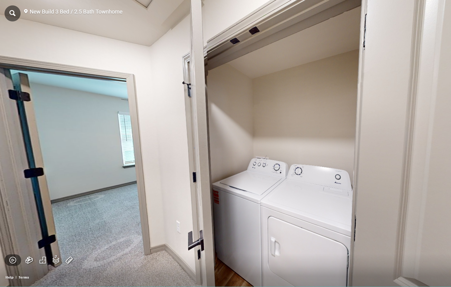 Laundry closet with stacked white washer and dryer next to an open doorway and hallway.