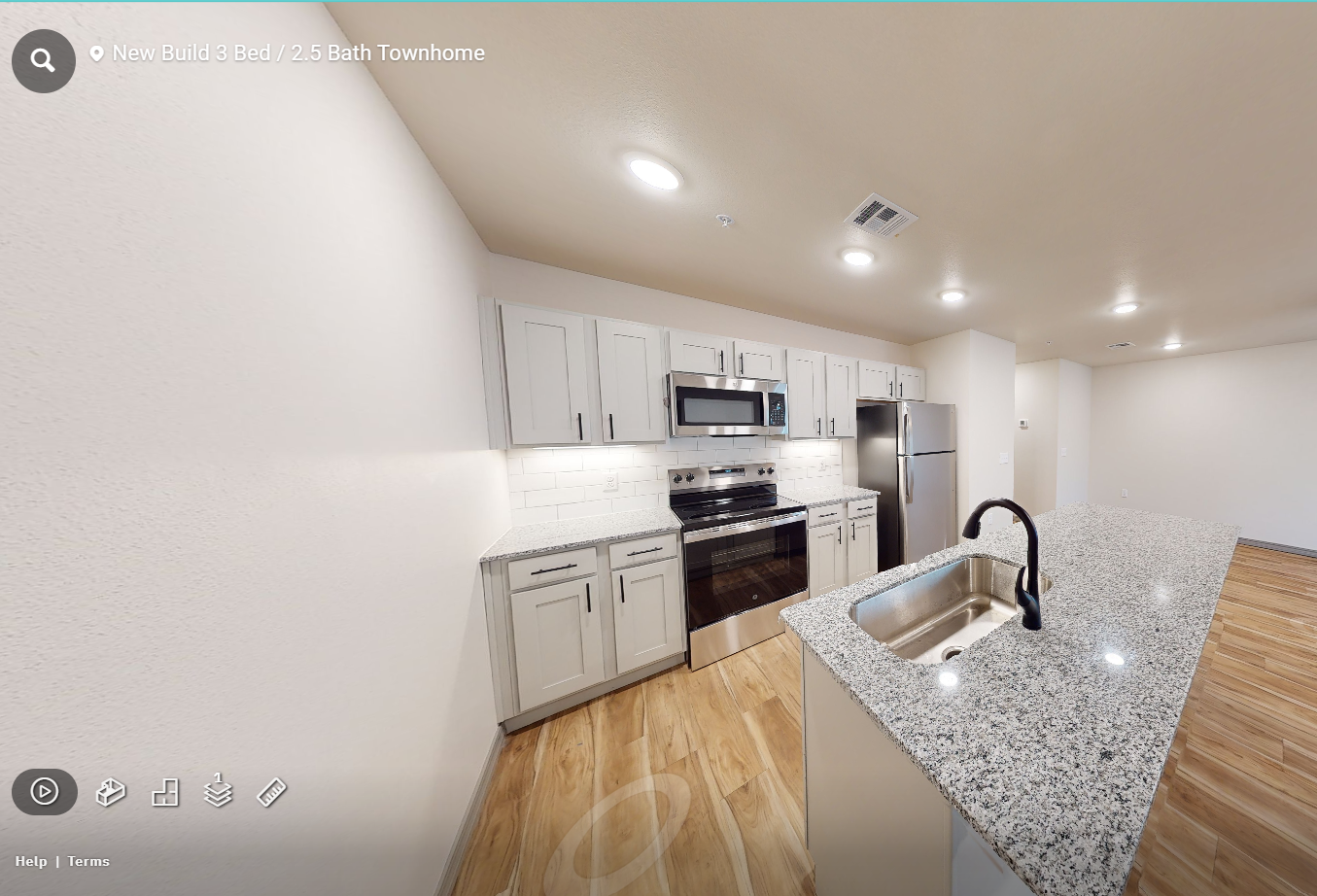 Modern kitchen with white cabinets, stainless appliances, and a granite island under recessed lights