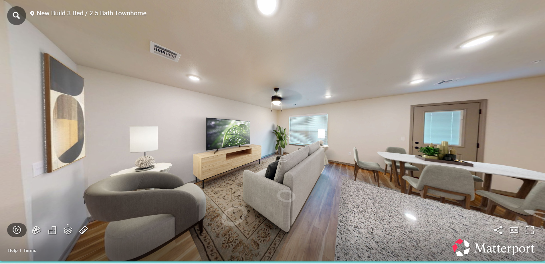 Bright modern living room with gray sofa, TV, wood console, and dining area by large windows