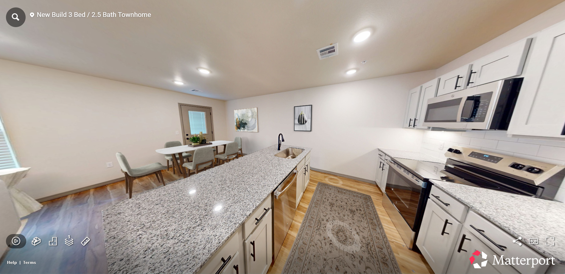 Bright kitchen with granite island, white cabinets, dining area, and patterned rug in open-plan home