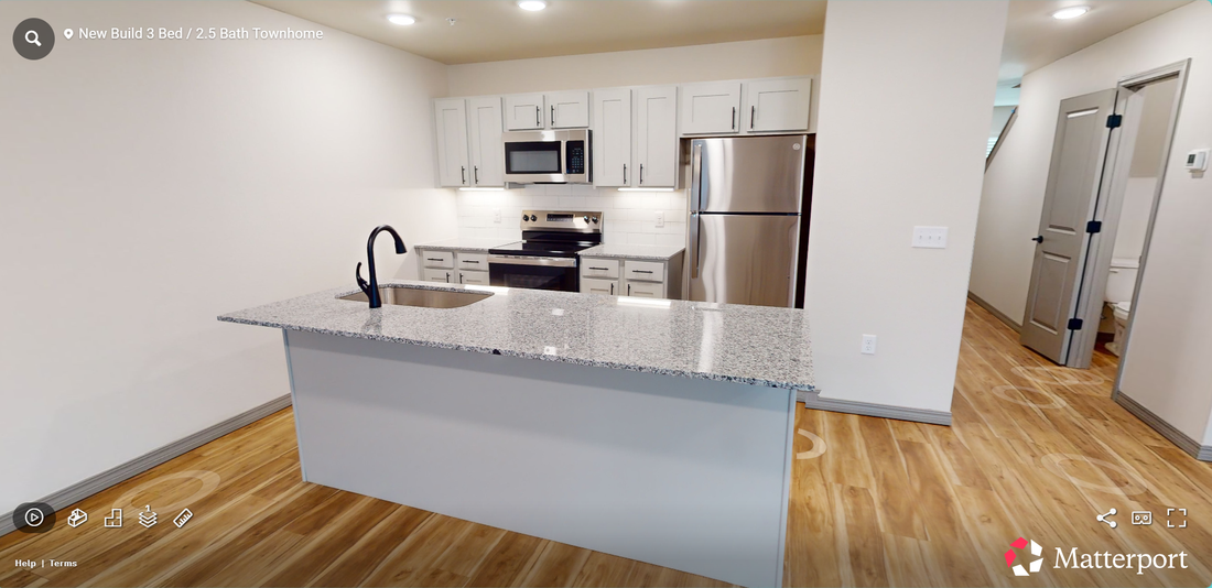 Open-plan kitchen with white cabinets, stainless appliances, and a gray granite island on hardwood floors