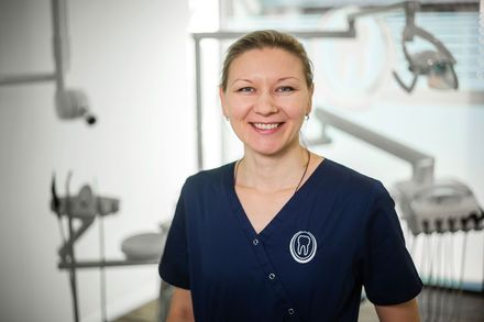 Eine Frau im blauen Kittel lächelt in einer Zahnarztpraxis.