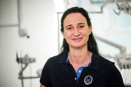 Eine Frau in einem blauen Hemd lächelt in einer Zahnarztpraxis.