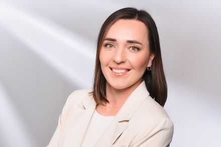 Eine Frau in einer weißen Jacke lächelt in die Kamera.