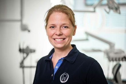 Eine Frau in einer Zahnarztpraxis lächelt in die Kamera.