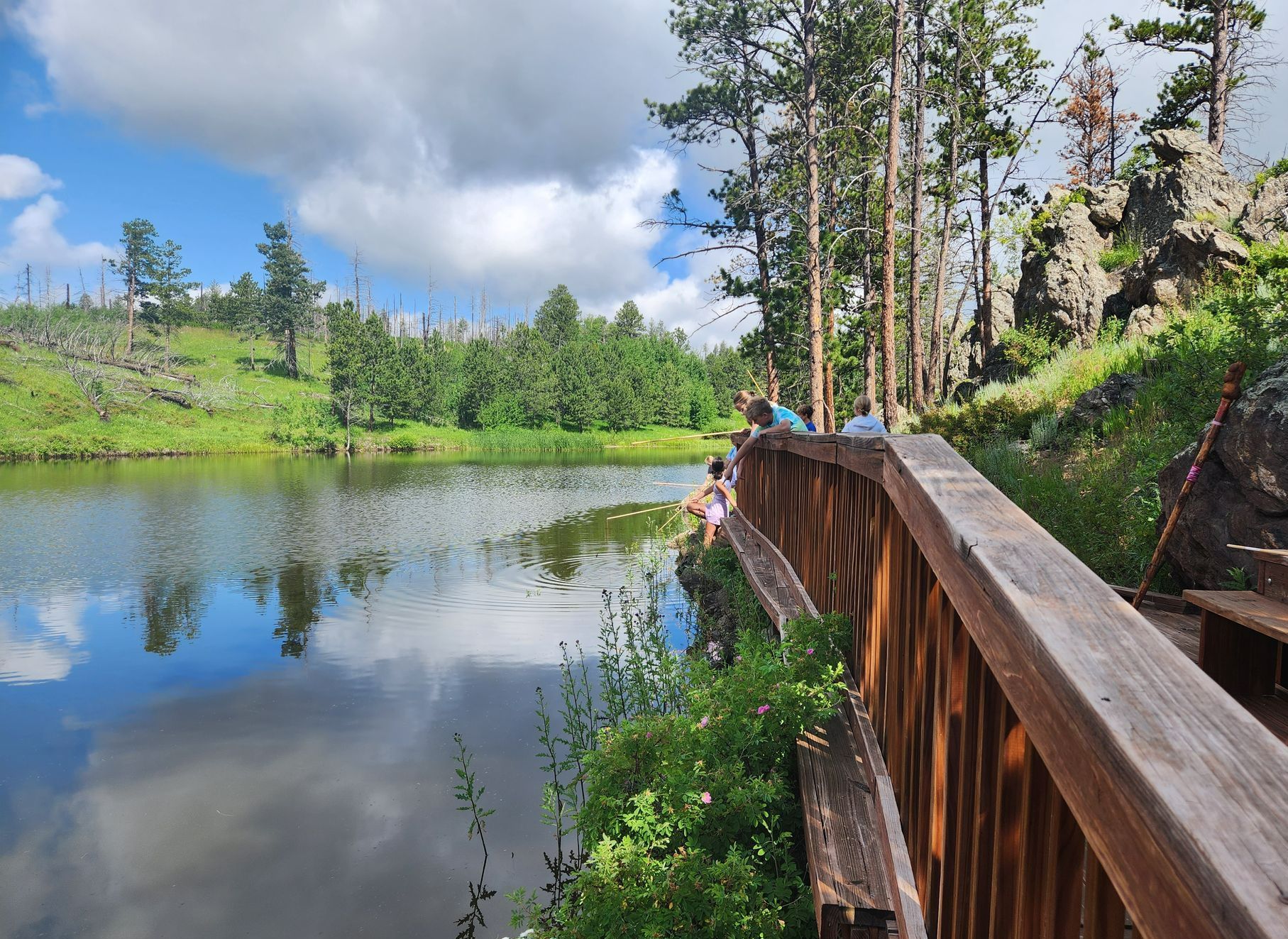 View of campers fishing from dock next to pond.