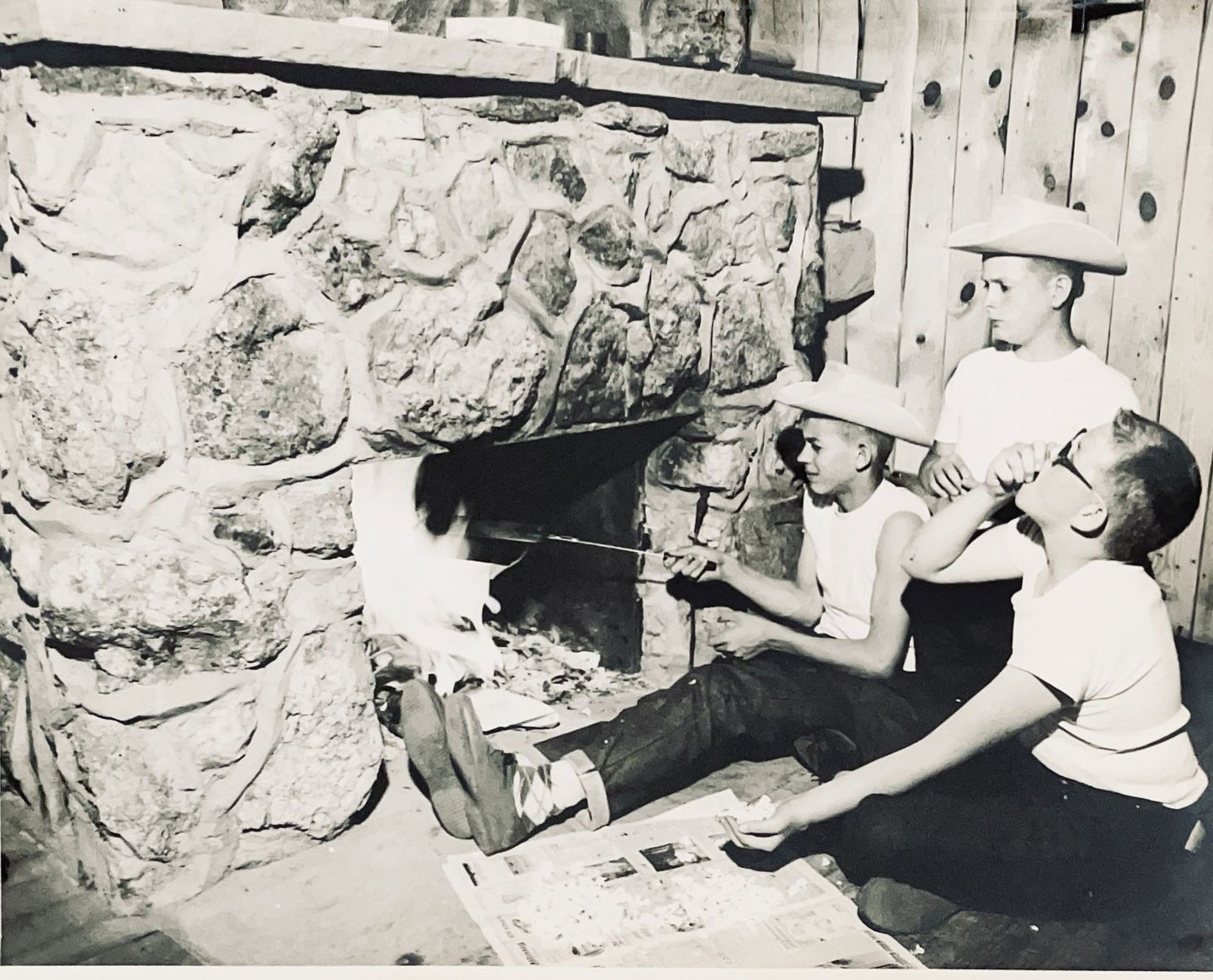Black and white image of boys sitting in front of fireplace with fire.