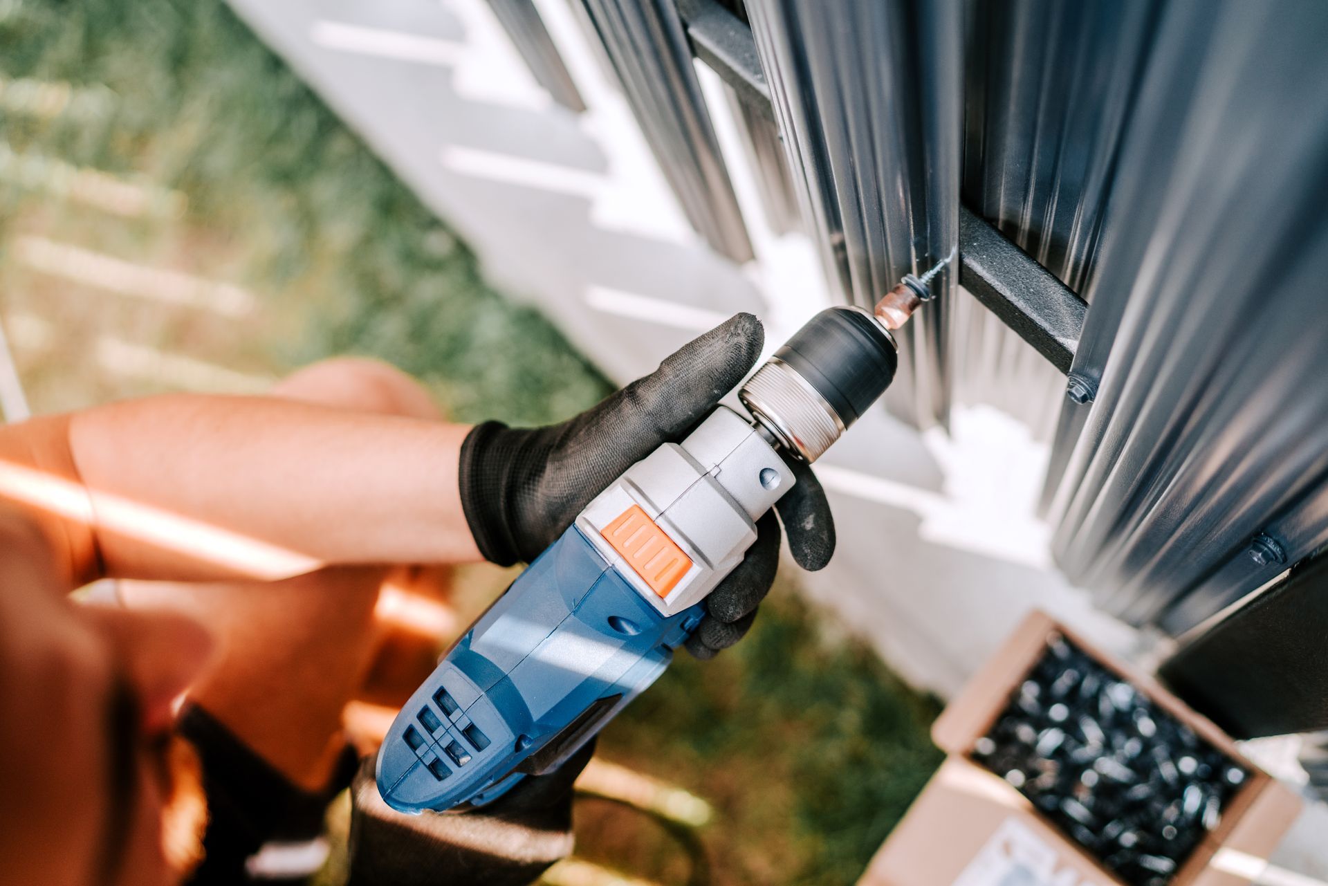 Person in black gloves using a blue drill to install a gray gutter
