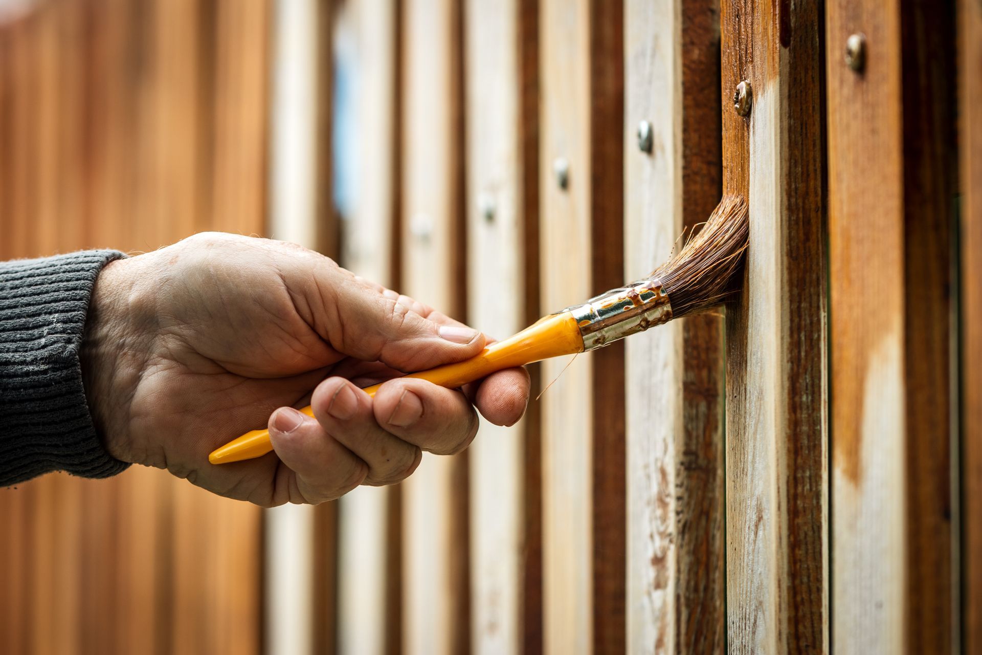 Hand painting a wooden fence with a paintbrush