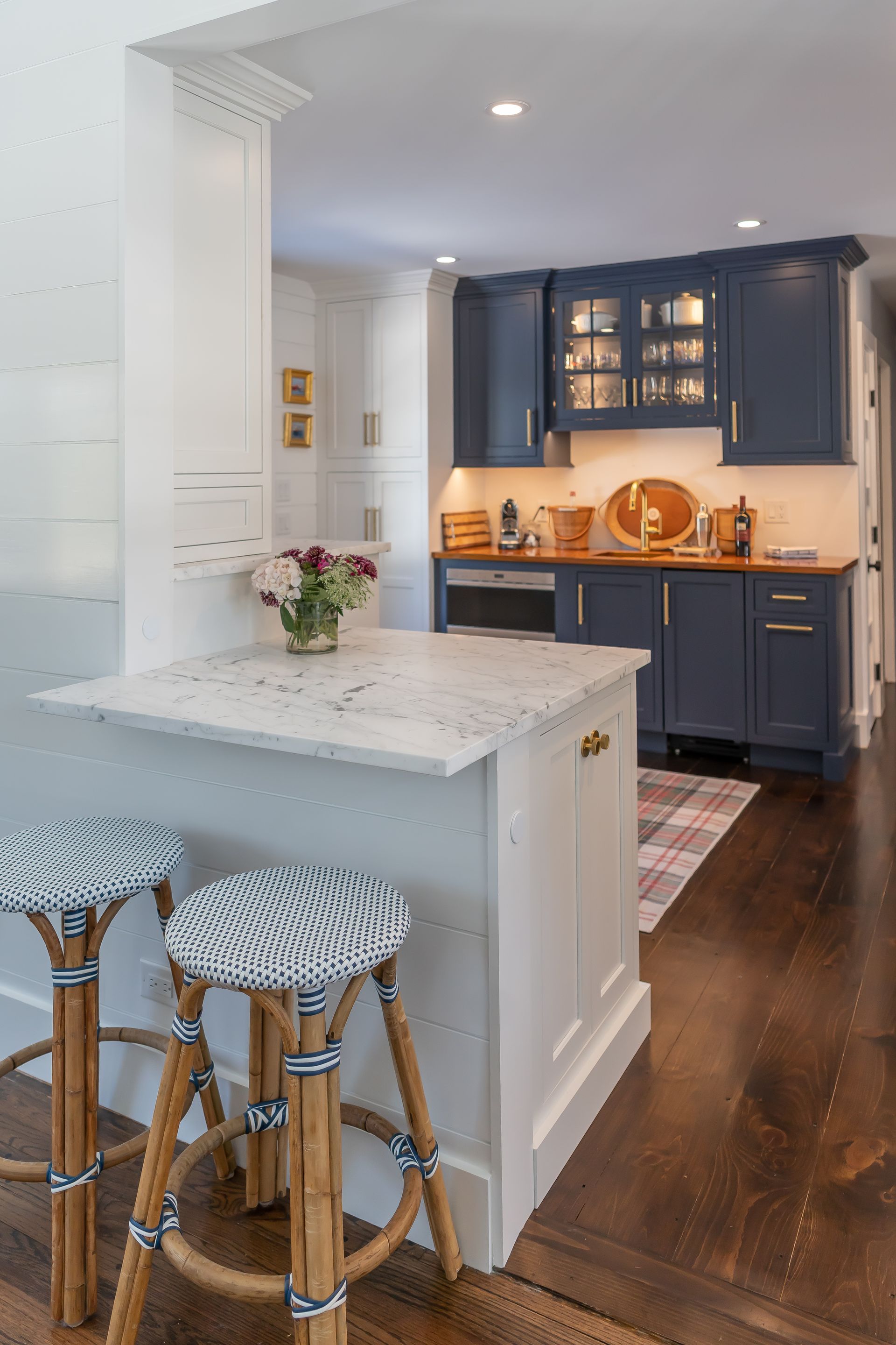 Bright kitchen with navy cabinets, white island, and two patterned stools beside a hardwood floor.