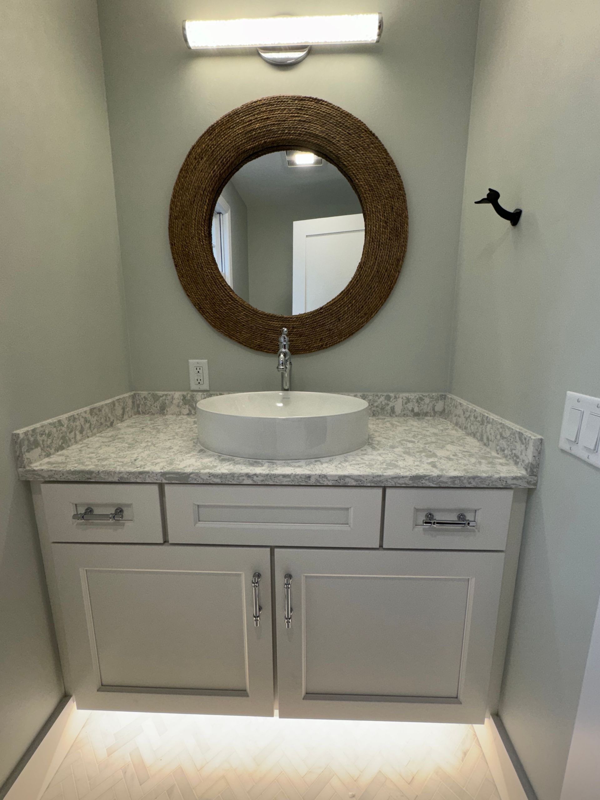 Small bathroom vanity with granite countertop, round mirror, and wall light in a narrow alcove.